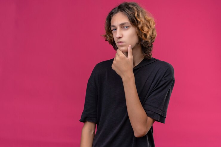 Foto gratuito chico pensativo con el pelo largo en camiseta negra agarró su barbilla en la pared rosa