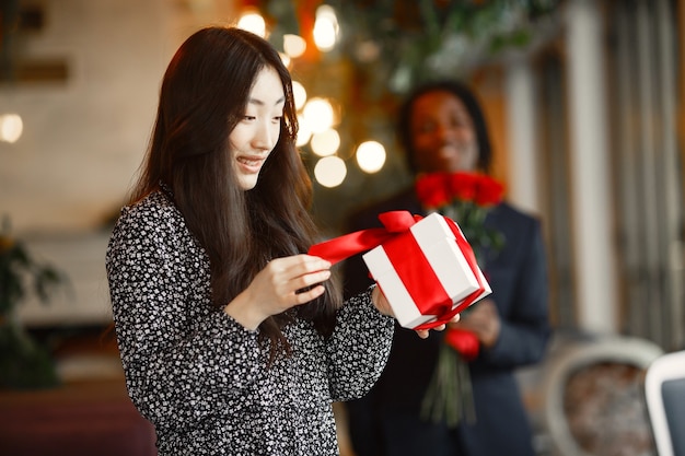 Chico de piel oscura con rosas. Niña feliz con un regalo. Velada romántica en un café.