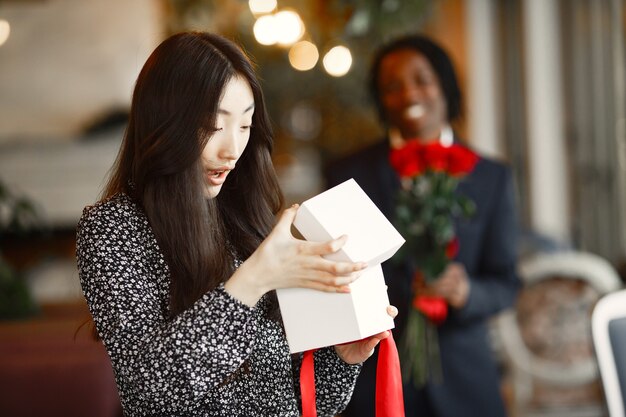 Chico de piel oscura con rosas. Niña feliz con un regalo. Velada romántica en un café.