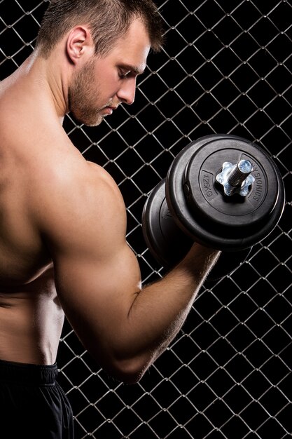 Chico poderoso con pesas que muestra los músculos en la valla
