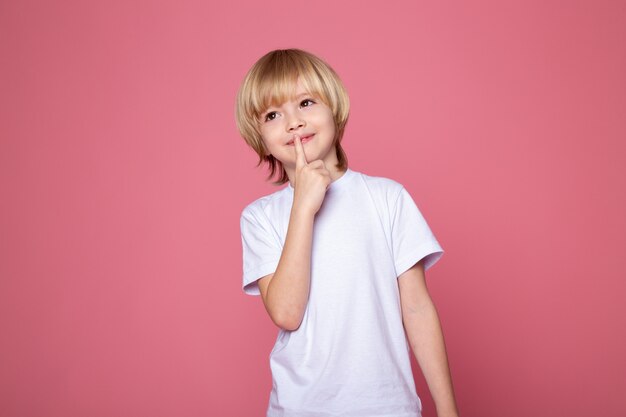 Chico posando niño pequeño con el dedo en los labios y la pared rosa