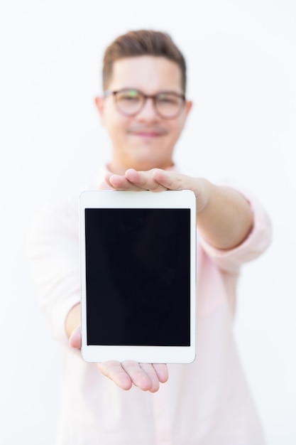 Foto gratuita chico positivo en anteojos que muestra la pantalla de la tableta en blanco