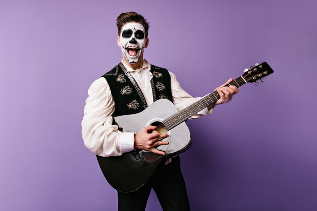 Chico positivo en traje tradicional mexicano canta serenata. Instantánea de hombre emocional con guitarra en sus manos.