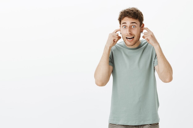 Foto gratuita chico preparándose para el big bang, cubriéndose los oídos sin escuchar ruido. estudiante masculino europeo divertido emocionado en camiseta casual