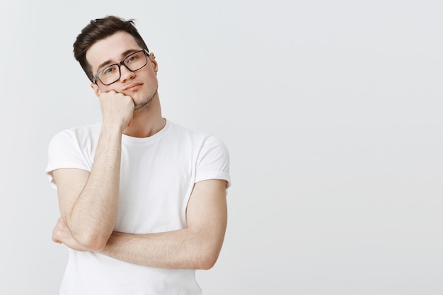 Chico reacio aburrido con gafas, apoyado en la mano y mirando sin interés