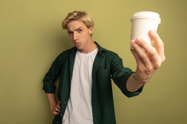 Chico rubio joven confiado con camiseta verde sosteniendo una taza de café