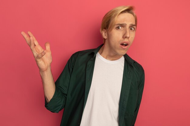 Chico rubio joven confundido con camiseta verde extendiendo la mano