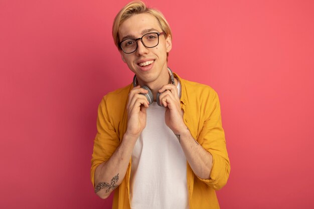 Chico rubio joven sonriente con camiseta amarilla y gafas con auriculares en el cuello