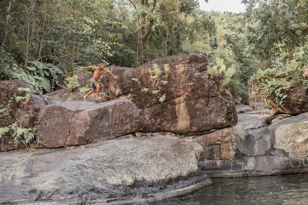 Foto gratuita el chico salta de una piedra al agua.