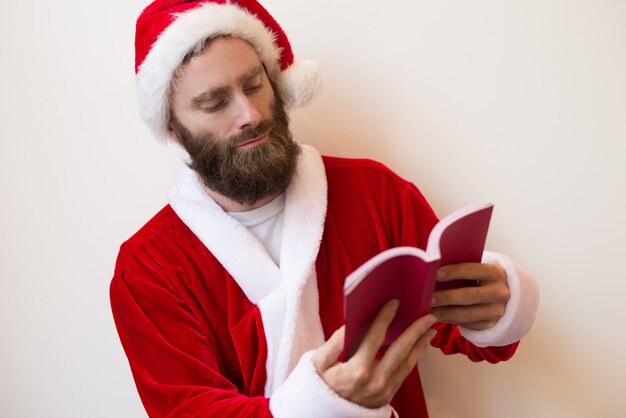 Chico serio con traje de Santa y libro de lectura