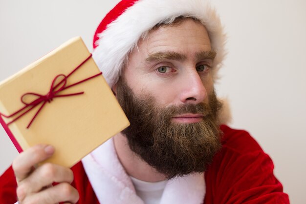 Chico serio con traje de Santa y sosteniendo la caja de regalo