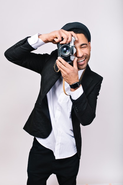 Chico sonriente alegre con sombrero, traje haciendo fotos en cámara, divirtiéndose. Hombre de moda, fotógrafo, turista feliz, pasatiempo encantador, ocio, persona emocionada, felicidad.