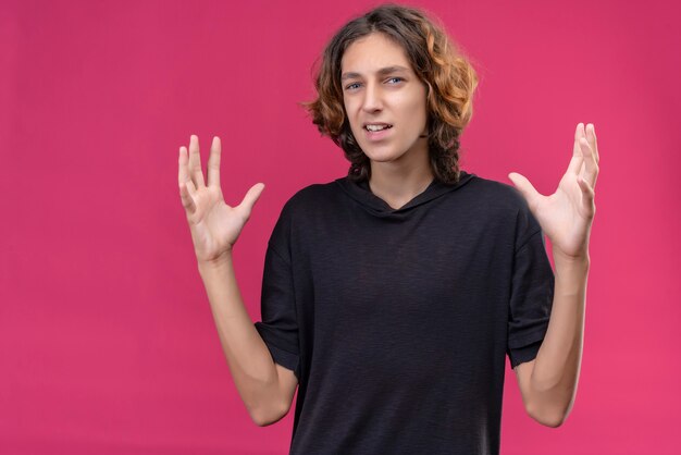 Chico sonriente con cabello largo en camiseta negra que muestra el tamaño en la pared rosa