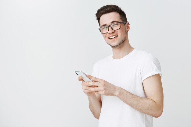 Chico sonriente feliz en gafas con teléfono móvil y mirando