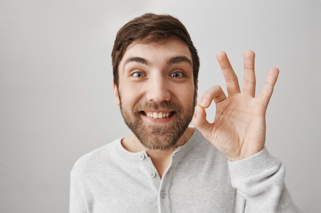 El chico sonriente lindo satisfecho muestra un gesto bien, recomienda el producto