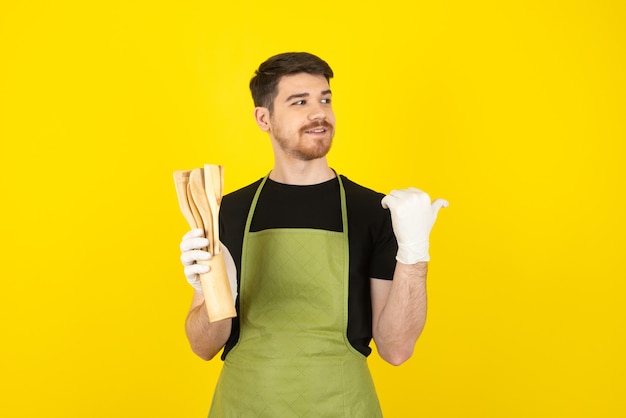 Chico sonriente sosteniendo cucharas de cocina de madera y mirando a otro lado en un amarillo.