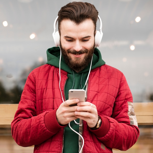 Chico sonriente de tiro medio con auriculares mirando smartphone