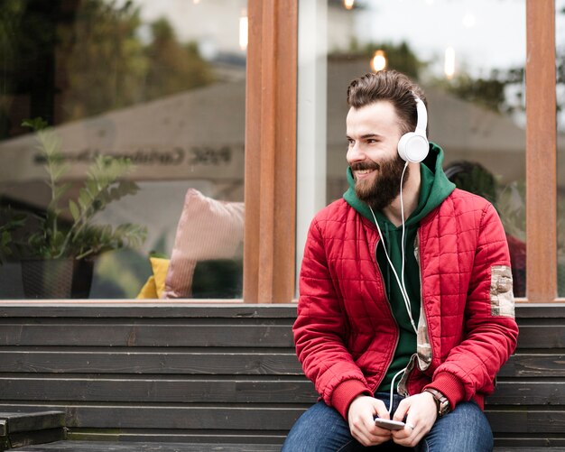 Chico sonriente de tiro medio con auriculares sentado en un banco