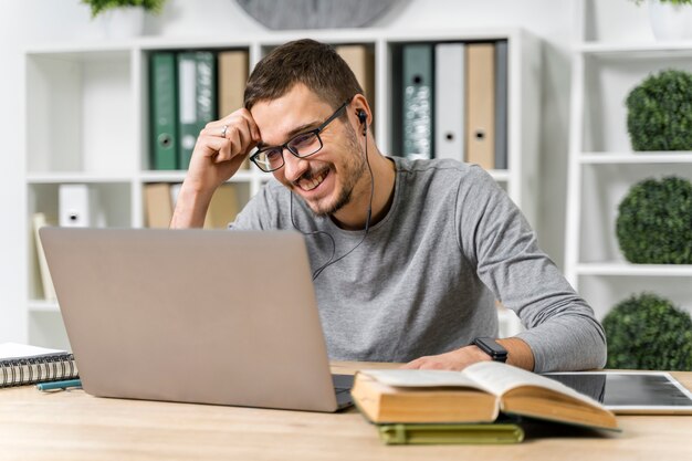 Chico sonriente de tiro medio estudiando con su computadora portátil