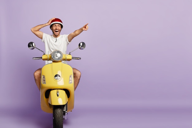 Chico sorprendido con casco conduciendo scooter amarillo