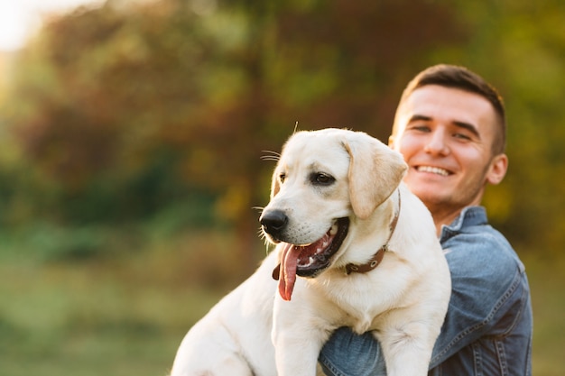 Chico sosteniendo a su perro amigo Labrador y sonriendo al atardecer