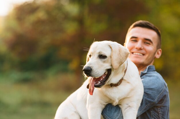 Chico sosteniendo a su perro amigo Labrador y sonriendo al atardecer