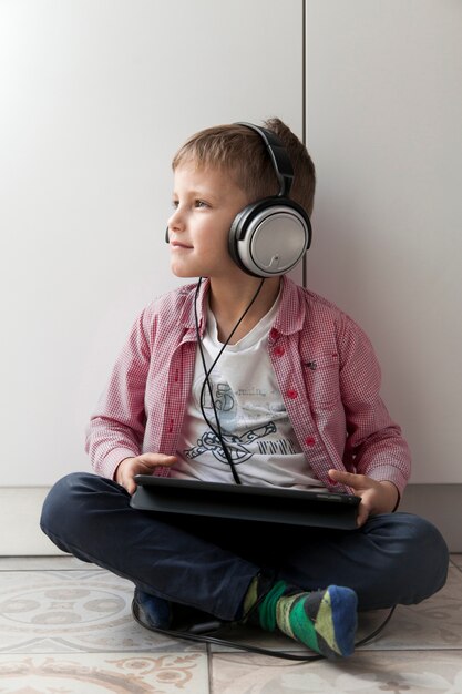 Chico con tableta escuchando música en el piso