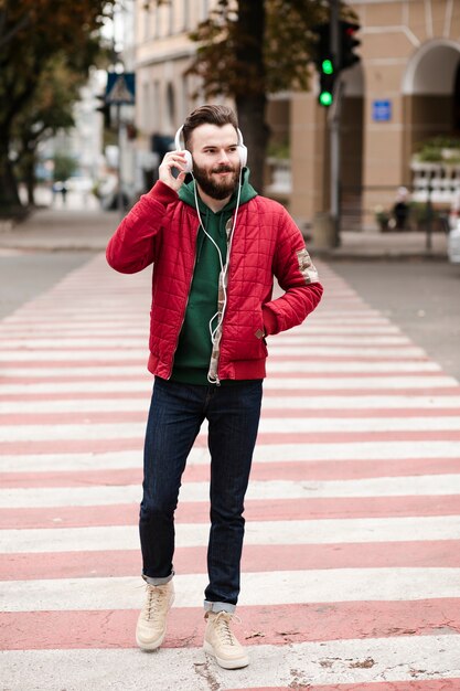 Chico de tiro completo con auriculares cruzando la calle