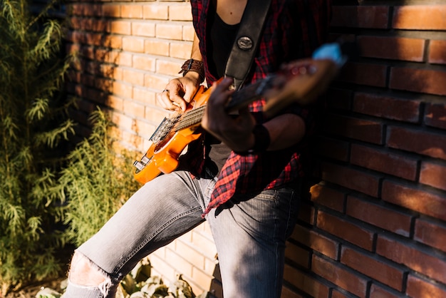 Chico tocando la guitarra eléctrica apoyándose en muro de ladrillo