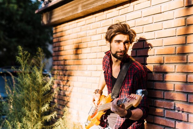 Chico tocando la guitarra eléctrica apoyándose en muro de ladrillo