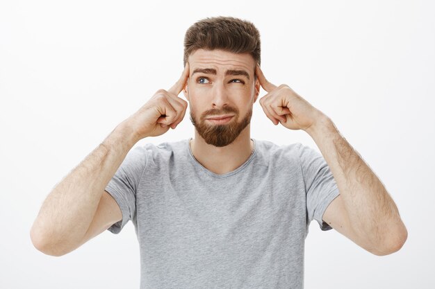 Chico tratando de concentrarse, pensar en un nuevo plan. Hombre carismático guapo, reflexivo y decidido, con barba y ojos azules entrecerrando los ojos, sonriendo con suficiencia sosteniendo los dedos en las sienes, enfocándose en un juego importante, concentrándose