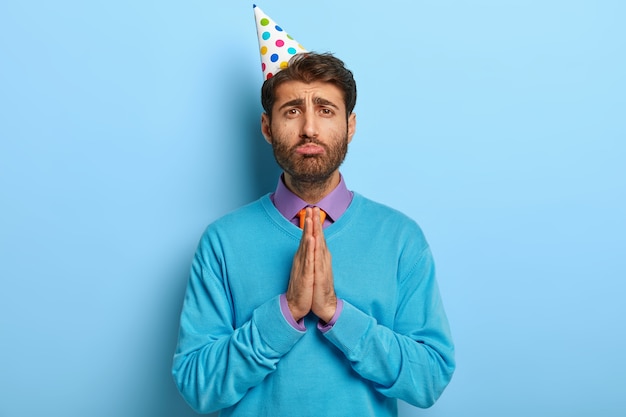 Chico triste con sombrero de cumpleaños posando en suéter azul