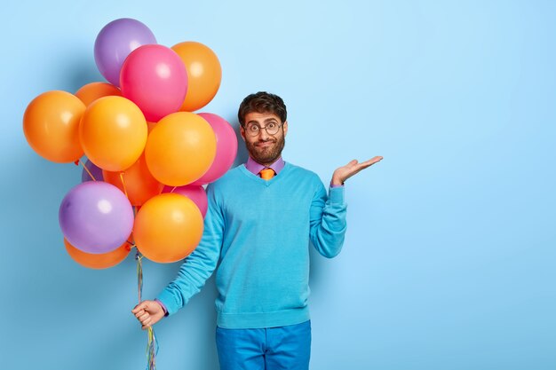 Chico vacilante confundido con globos posando en suéter azul