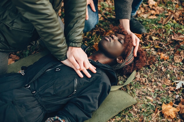 Los chicos ayudan a una mujer. Niña africana yace inconsciente. Brindar primeros auxilios en el parque.