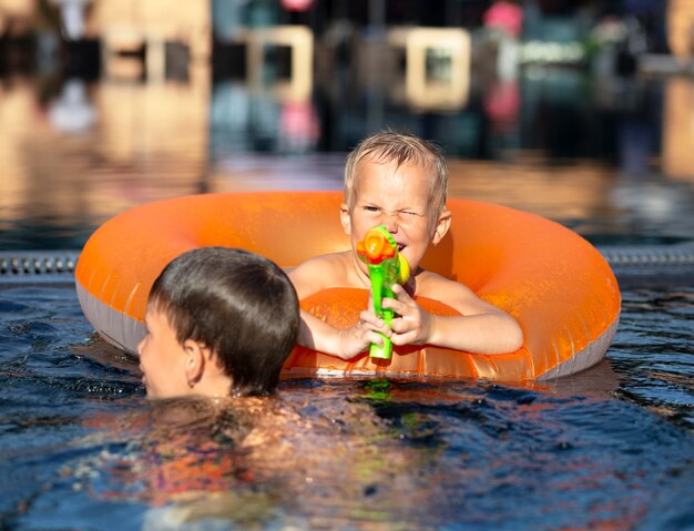 Chicos divirtiéndose en la piscina con flotador y pistola de agua.