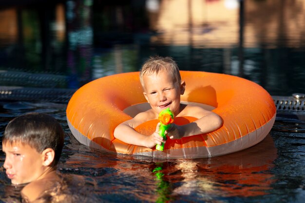 Chicos divirtiéndose en la piscina con flotador y pistola de agua.