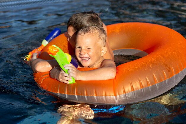 Chicos divirtiéndose en la piscina con flotador y pistola de agua.