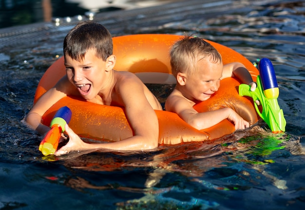 Chicos divirtiéndose en la piscina con flotador y pistola de agua.