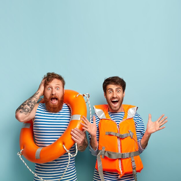 Chicos emocionados en exceso posando en la playa con chaleco salvavidas y aro salvavidas