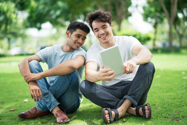 Chicos guapos alegres estudiantes viendo video en tableta