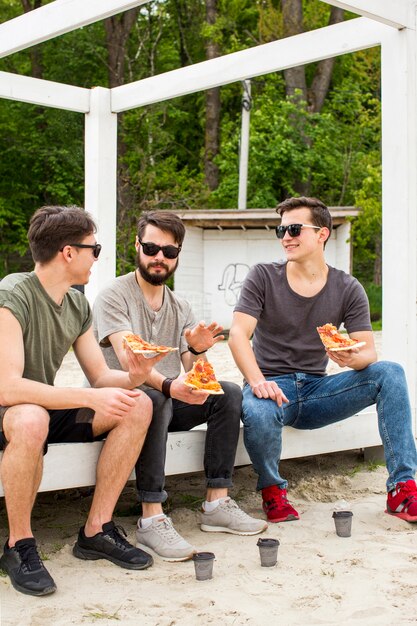 Chicos jóvenes hablando mientras sostienen pizza en reposo