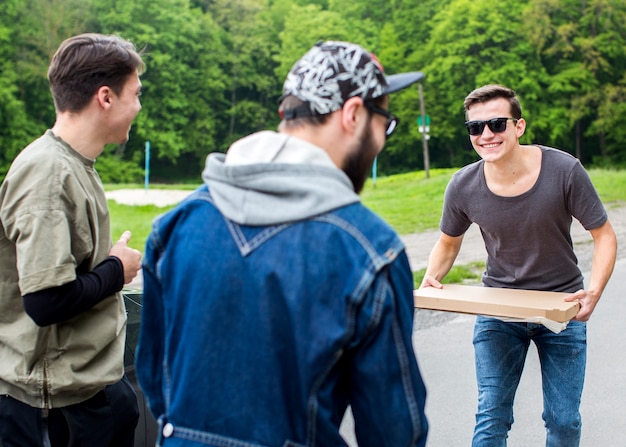 Foto gratuita chicos jóvenes positivos con pizza en el parque