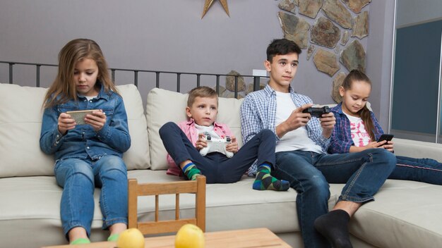 Chicos jugando videojuegos y chicas usando teléfonos inteligentes