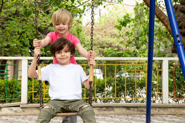 Chicos lindos adorables en el patio interior balanceándose en los columpios