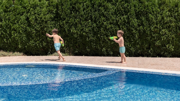 Chicos en la piscina jugando con pistola de agua