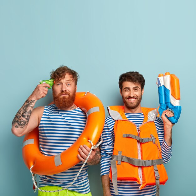 Chicos serios posando en la playa con chaleco salvavidas y aro salvavidas