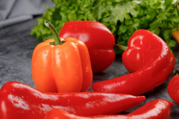 Chiles rojos con un pimiento amarillo y algo de vegetación alrededor.