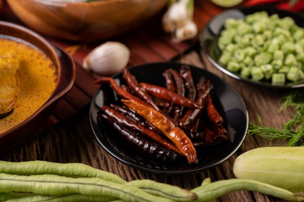 Chiles secos fritos en un plato negro con lentejas. Los pepinos y el ajo se colocan sobre la mesa de madera.