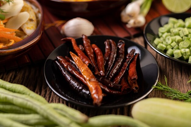 Chiles secos fritos en un plato negro con lentejas. Los pepinos y el ajo se colocan sobre la mesa de madera.