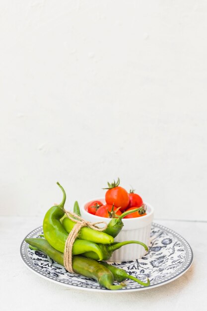 Chiles verdes y cuenco de tomates rojos en la placa de cerámica contra el fondo blanco